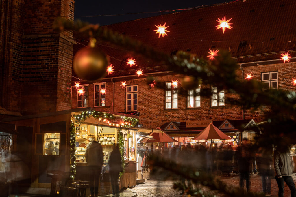 Weihnachtsbuden unter einem roten Sternenhimmel und im Hintergrund das Backstein Gebäude des Kanzleigebäudes