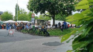 Blick auf den Eingang vom Wochenmarkt am Brink mit Sicht auf den Grünstreifen voller Menschenund Musiker und dahinter der Kaffeewagen und die andern Marktwagen
